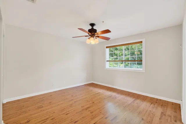 an empty room with wooden floor ceiling fan and windows