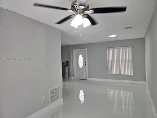 a view of an empty room with window and chandelier fan