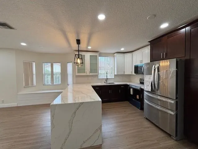 a large kitchen with stainless steel appliances kitchen island granite countertop a refrigerator a sink dishwasher a stove and a refrigerator with wooden floor
