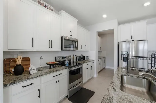 a kitchen with granite countertop a sink stainless steel appliances and white cabinets