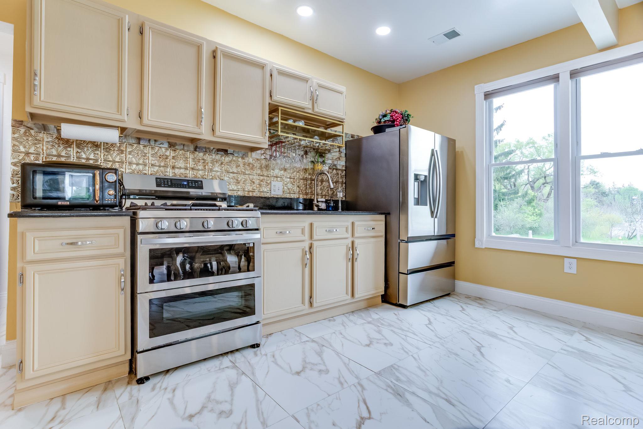 2400 North Lakeshore Road Carsonville, MI 48419 - Photo 14 of 33 Kitchen with stainless steel appliances, cream cabinetry, light marble finish flooring, backsplash, and dark stone counters