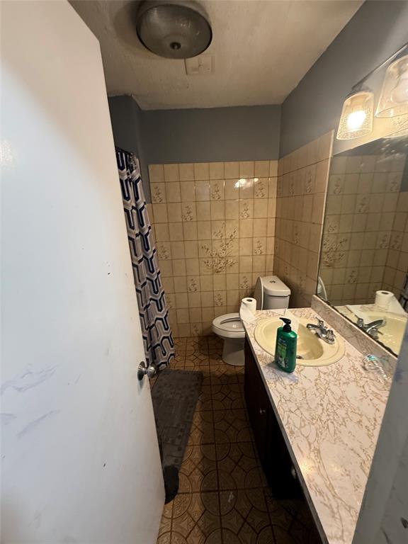 6036 Harrison Way Watauga, TX 76148 - Photo 29 of 39 Full bath featuring vanity, a shower with shower curtain, tile walls, and dark tile patterned floors