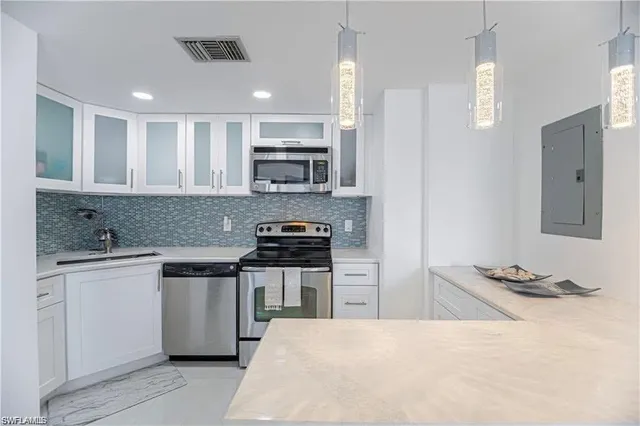 a kitchen with stainless steel appliances granite countertop a stove top oven a sink a refrigerator white cabinets and wooden floor