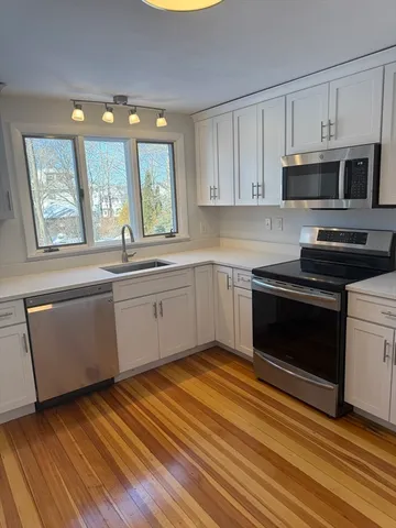 a kitchen with stainless steel appliances granite countertop a sink cabinets and a wooden floor