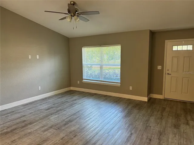 an empty room with wooden floor a ceiling fan and windows