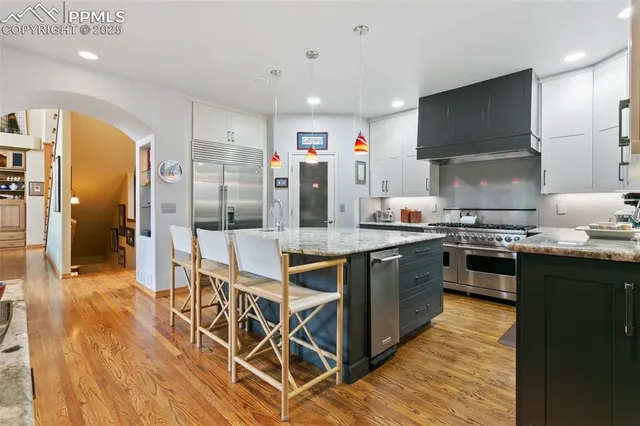 a kitchen with stainless steel appliances granite countertop a stove top oven a sink dishwasher a refrigerator and white cabinets with wooden floor