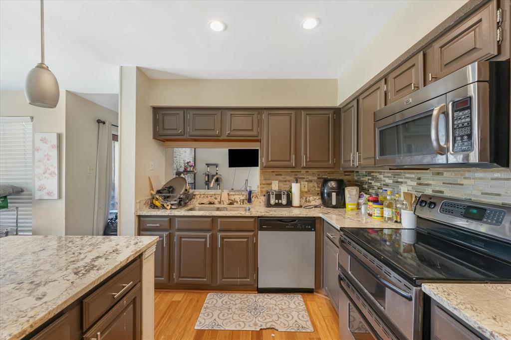 1301 Memory Lane, Unit 4924 Arlington, TX 76011 - Photo 4 of 19 Kitchen with appliances with stainless steel finishes, light wood-type flooring, pendant lighting, and light stone counters