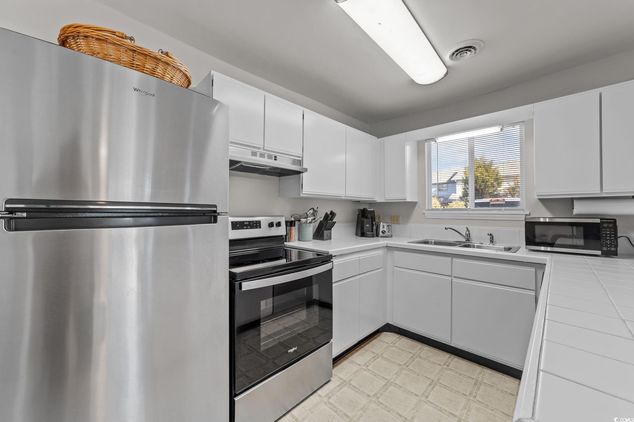 3700 Golf Colony Lane, Unit 2I Little River, SC 29566 - Photo 10 of 23 Kitchen featuring stainless steel appliances, tile countertops, white cabinetry, light flooring, and under cabinet range hood