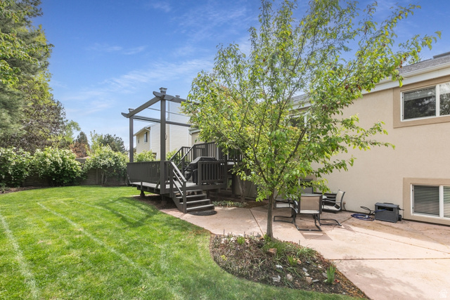 10183 Hickory Point Drive Sandy, UT 84092 - Photo 35 of 36 Expansive backyard featuring a manicured lawn, a raised wood-finish deck with a pergola, a ground-level concrete patio, and mature trees