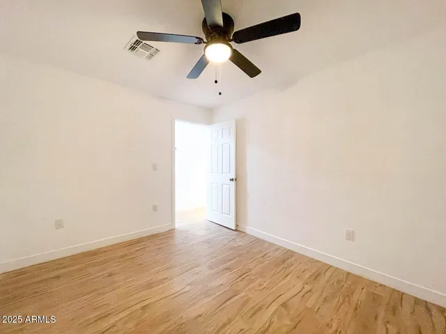 an empty room with wooden floor ceiling fan and window