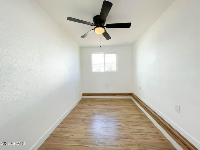 a view of empty room with wooden floor and fan