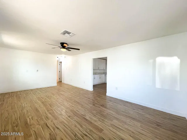 an empty room with wooden floor ceiling fan and windows