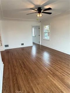 an empty room with wooden floor chandelier fan and windows