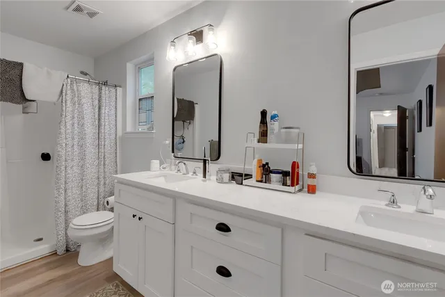 a bathroom with double vanity sink a toilet a mirror and shower
