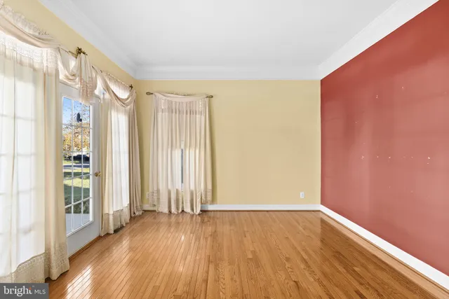 an empty room with wooden floor and windows with curtains
