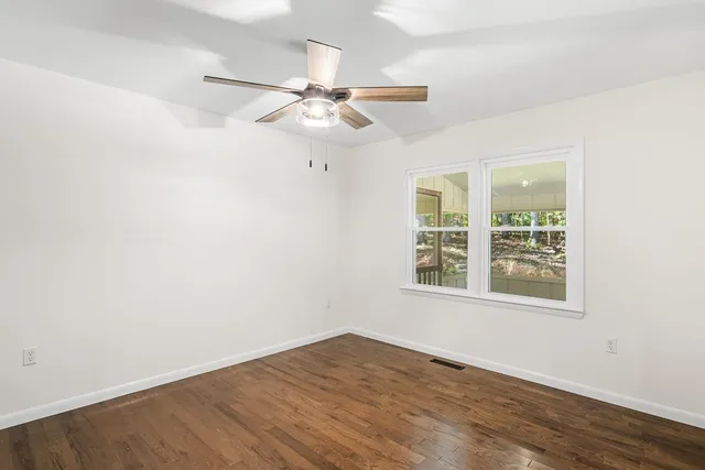 an empty room with wooden floor fan and windows