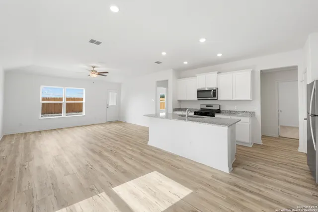 a kitchen with granite countertop a stove top oven a sink and white cabinets with wooden floor