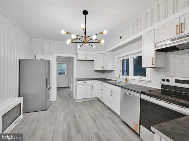 a large kitchen with stainless steel appliances granite countertop a refrigerator a sink dishwasher a stove and white cabinets with wooden floor