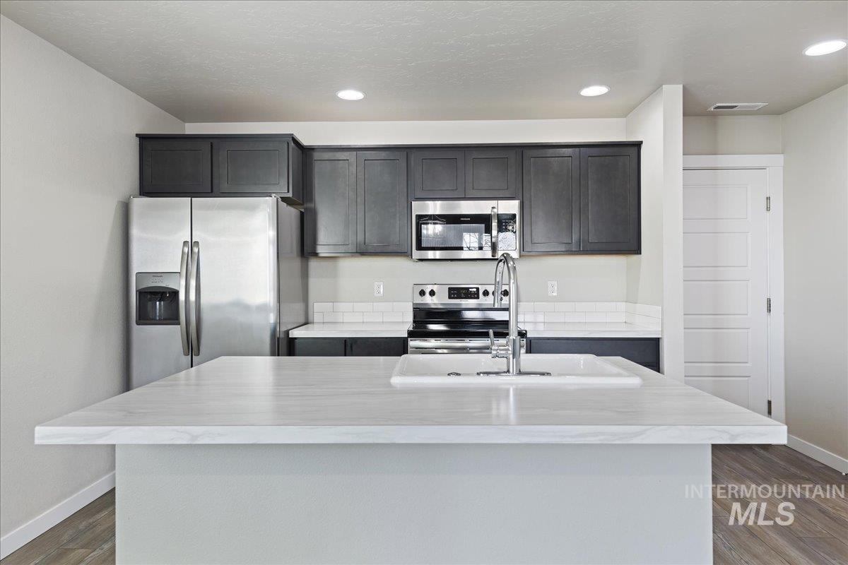 2487 East Goldstone Street Meridian, ID 83642 - Photo 8 of 25 Kitchen featuring stainless steel appliances, dark wood-type flooring, a kitchen island with sink, and recessed lighting