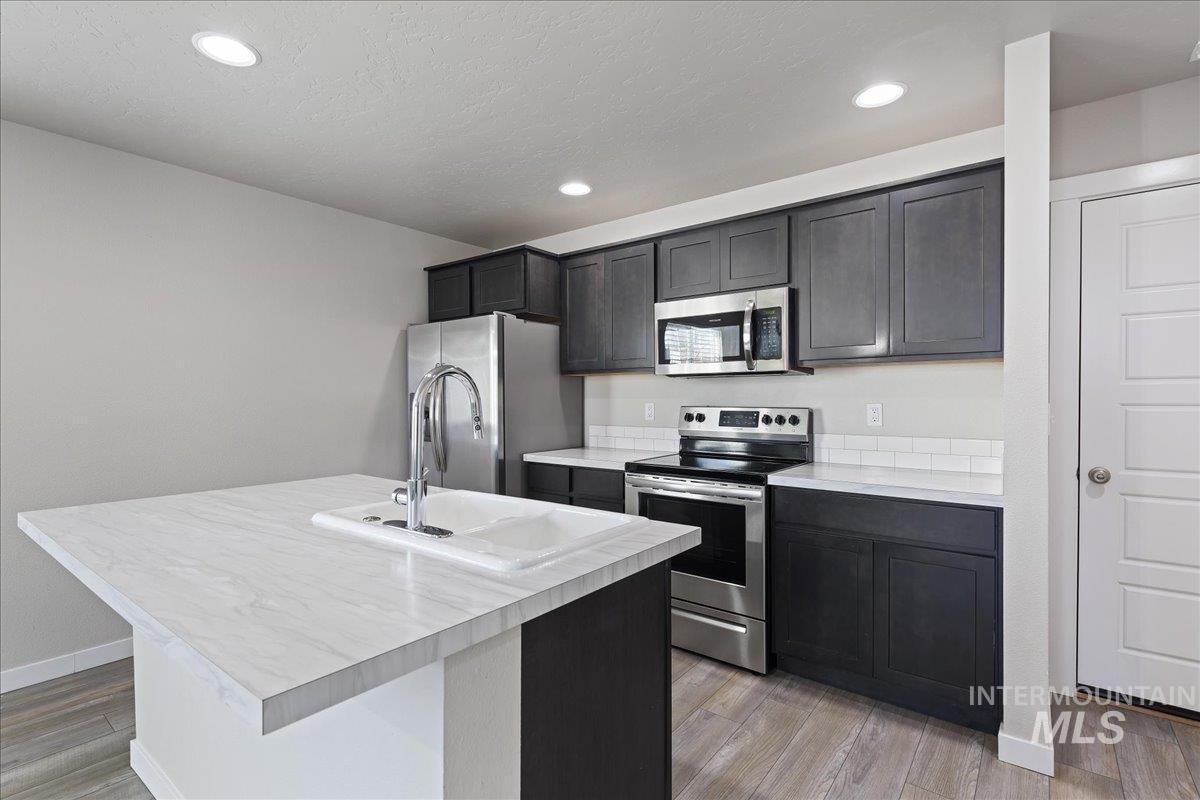 2487 East Goldstone Street Meridian, ID 83642 - Photo 9 of 25 Kitchen with stainless steel appliances, light countertops, light wood finished floors, a kitchen island with sink, and recessed lighting