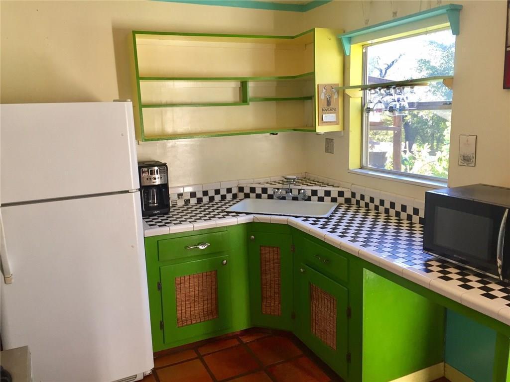 1614 Elmira Road Austin, TX 78721 - Photo 17 of 23 Kitchen with tile counters, freestanding refrigerator, open shelves, black microwave, and green cabinetry
