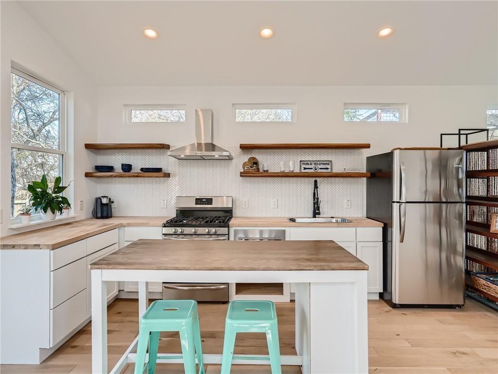 1614 Elmira Road Austin, TX 78721 - Photo 4 of 23 Kitchen featuring butcher block countertops, tasteful backsplash, stainless steel appliances, wall chimney exhaust hood, and plenty of natural light