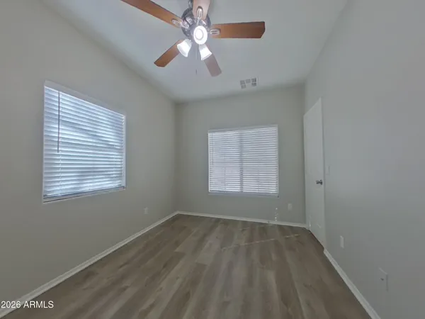 an empty room with wooden floor chandelier fan and windows