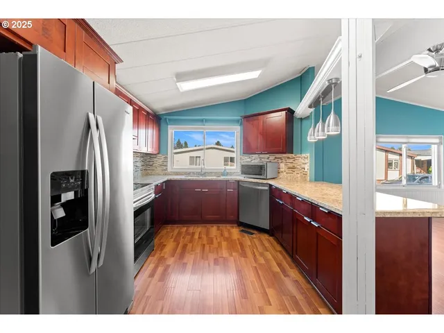 a kitchen with stainless steel appliances granite countertop a refrigerator a stove and a sink with wooden cabinets