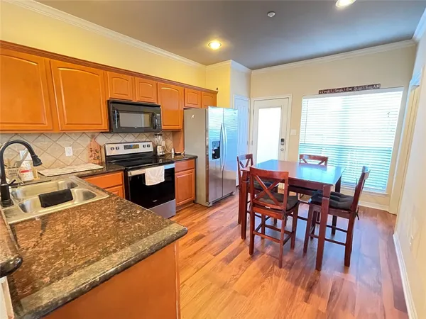 a kitchen with stainless steel appliances granite countertop a stove top oven a sink dishwasher a dining table and chairs with wooden floor