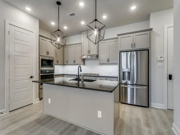 a kitchen with stainless steel appliances granite countertop a refrigerator a oven a sink a stove a dining table and chairs with wooden floor