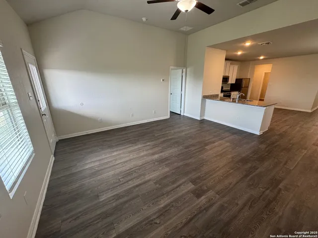 an empty room with wooden floor and kitchen view