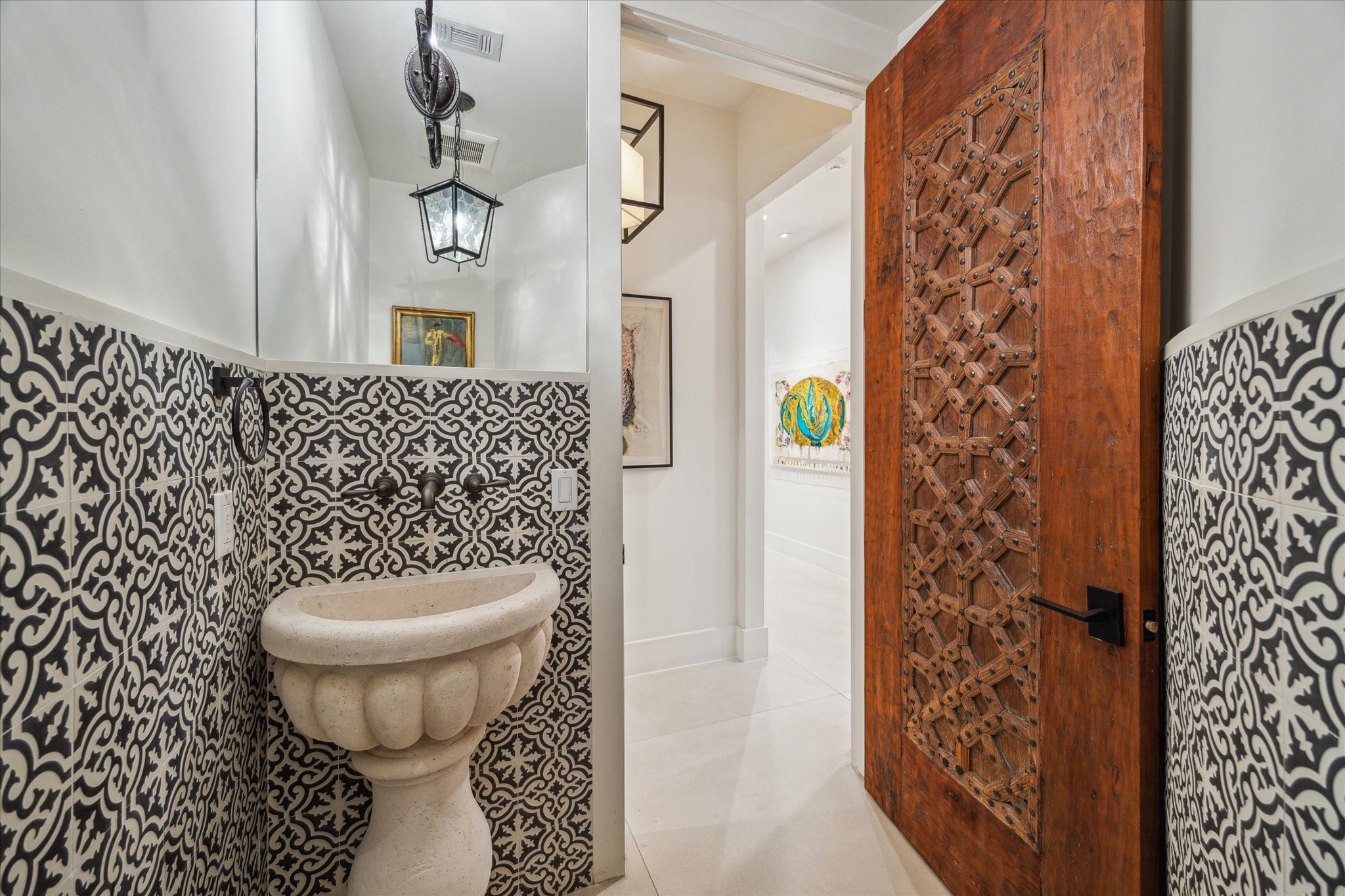 3214 Westheimer Road Houston, TX 77098 - Photo 20 of 39 The powder room exudes charm with its antique carved wood door, black-and-white cement tile wainscoting, and a carved stone pedestal sink. Antique lighting fixtures add a touch of elegance to this uniquely designed space. It’s a showstopper for guests.