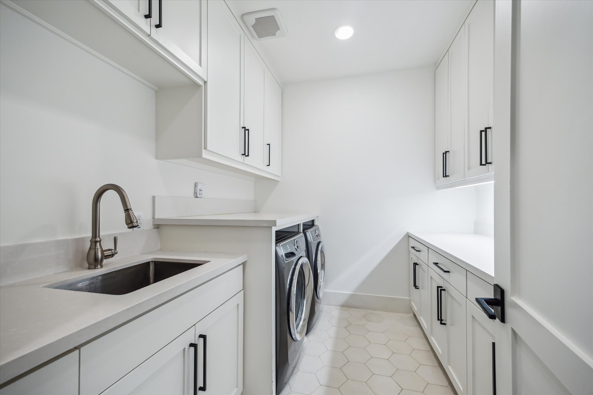 3214 Westheimer Road Houston, TX 77098 - Photo 36 of 39 A built-in sink sits beside the under-counter washer and dryer, with ample folding space above. Recessed can lights overhead and under-counter lighting below highlight the clean lines of the cabinetry. Hexagonal tile flooring grounds the room.