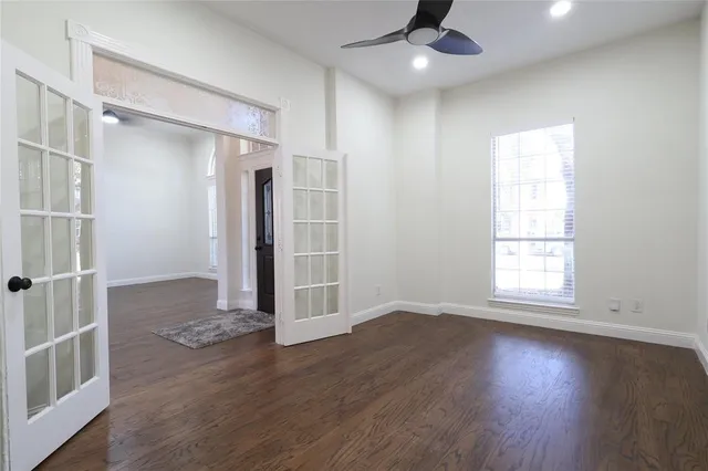 an empty room with wooden floor a ceiling fan and windows