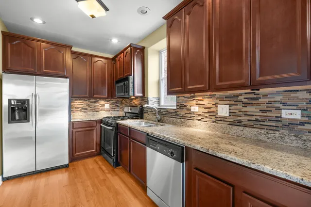 a kitchen with stainless steel appliances granite countertop a sink a stove a refrigerator cabinets and wooden floor