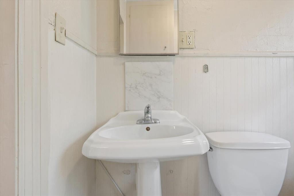608 9th Street Hico, TX 76457 - Photo 13 of 23 White pedestal sink with chrome faucet, complemented by a white toilet and beadboard wainscoting