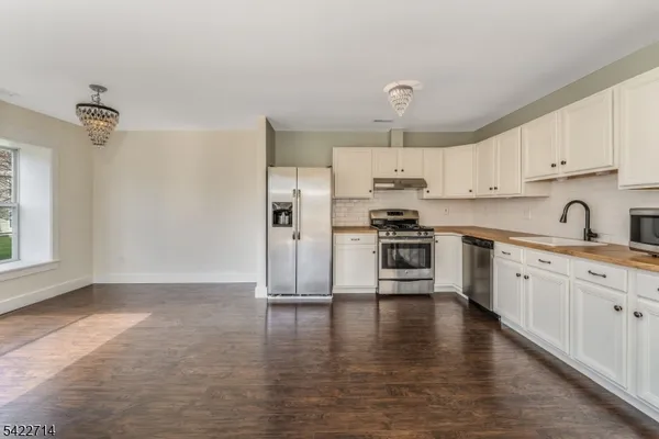a kitchen with granite countertop a refrigerator oven a sink and white cabinets
