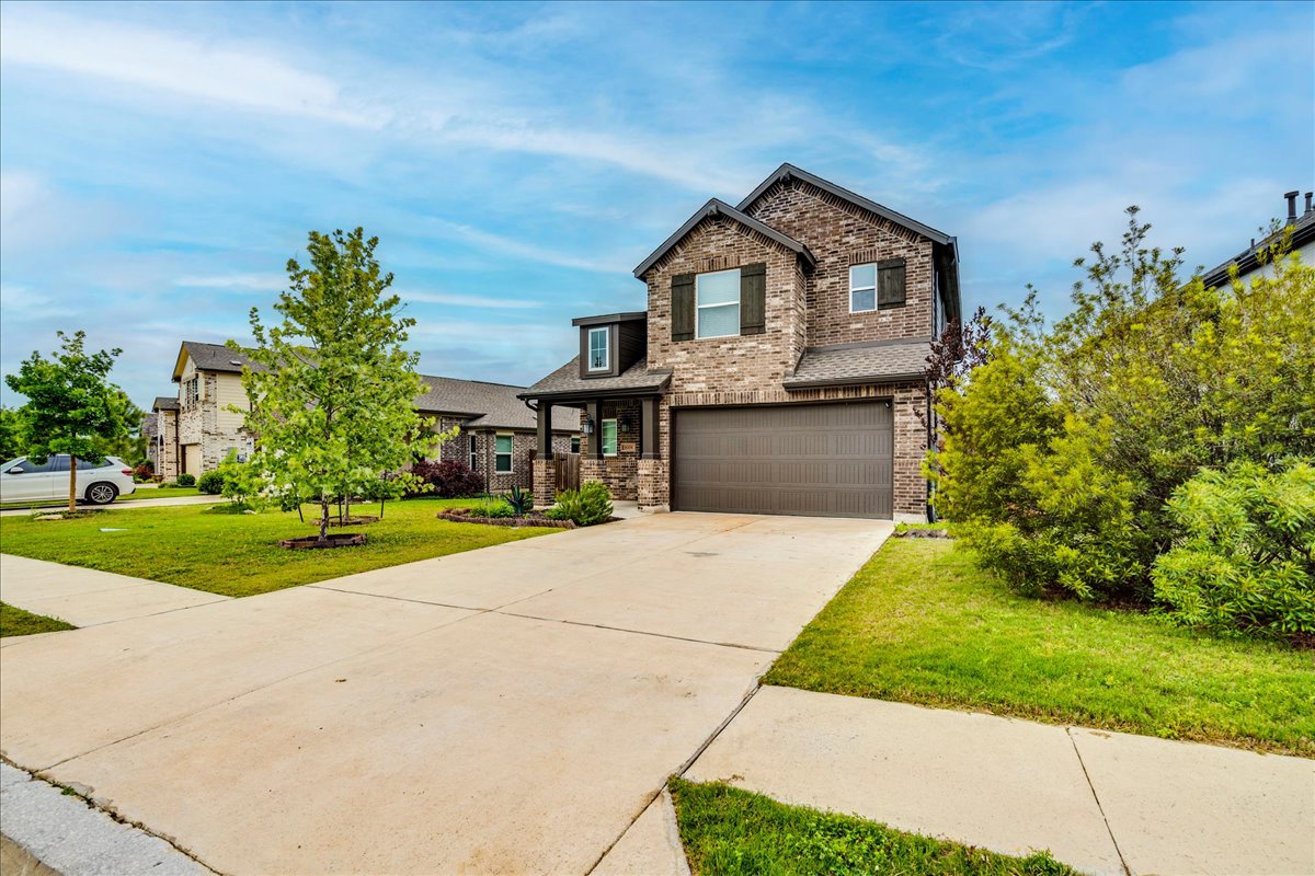 8008 Prairie Rye Drive Lago Vista, TX 78645 - Photo 18 of 40 Two-story brick exterior featuring a multi-pane window with dark shutters, an attached garage, a concrete driveway, and a manicured lawn with established plantings