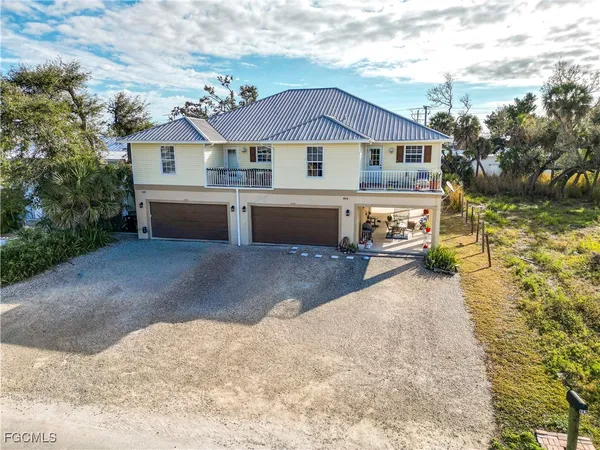 a view of a white house with a yard plants and large tree