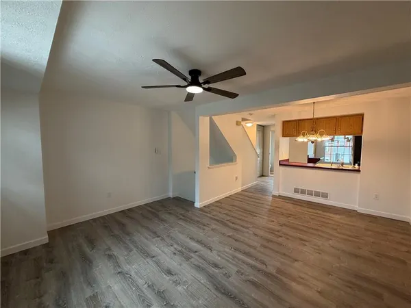 an empty room with wooden floor chandelier fan and windows