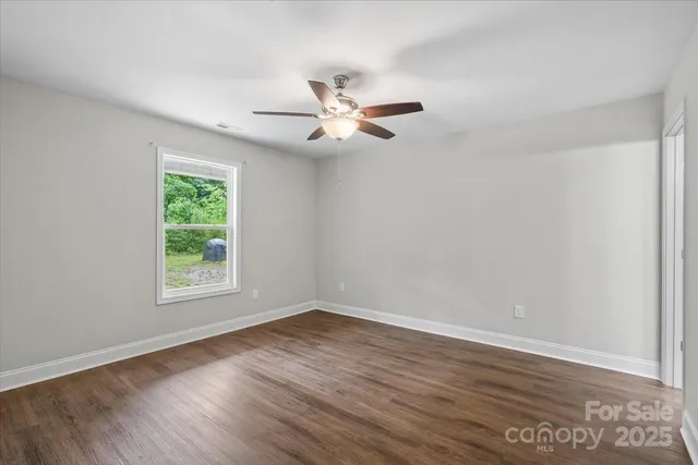 an empty room with wooden floor ceiling fan and window