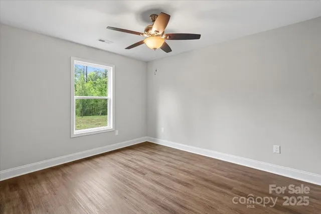 an empty room with wooden floor fan and windows