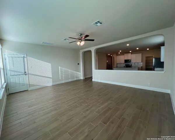 an empty room with wooden floor and a kitchen