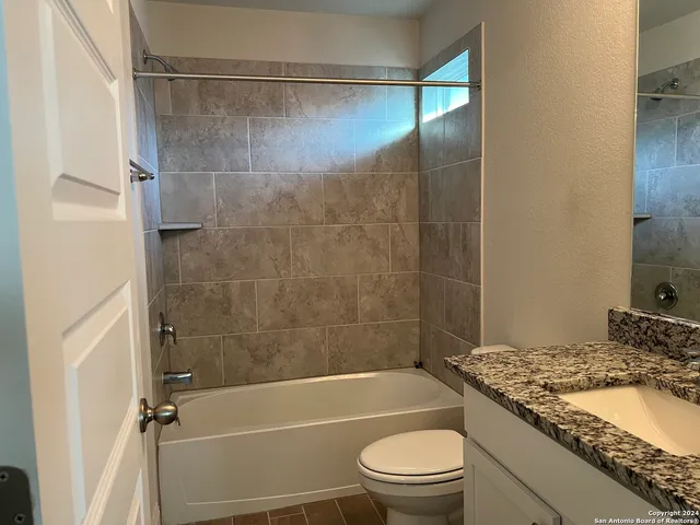 a bathroom with a granite countertop bathtub shower sink vanity and toilet