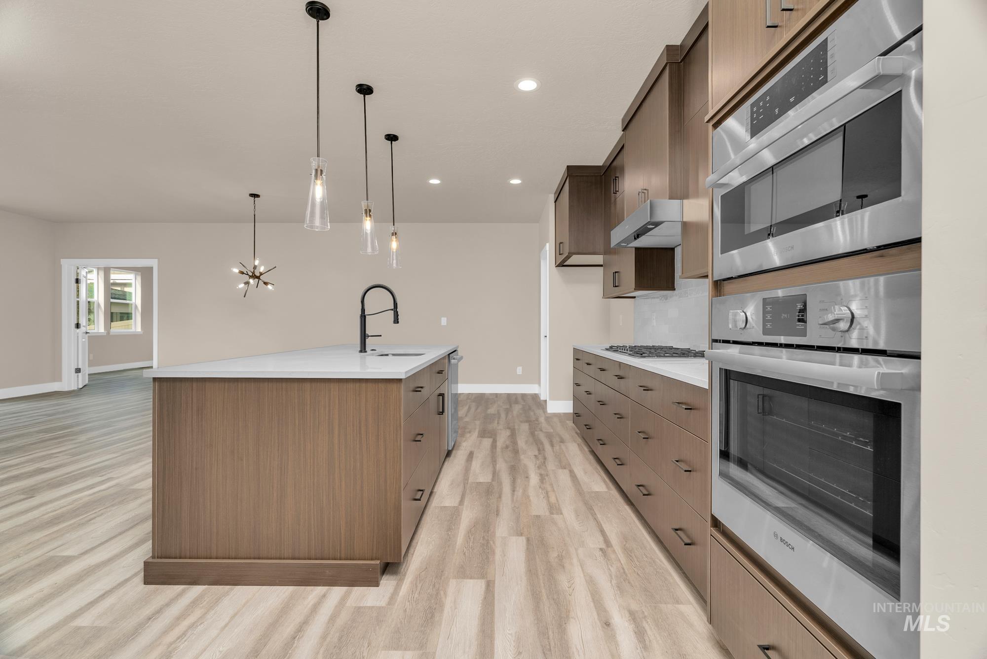 2848 West Jutland Street Meridian, ID 83642 - Photo 3 of 25 Kitchen with stainless steel appliances, a center island with sink, light wood finished floors, a chandelier, and light stone countertops