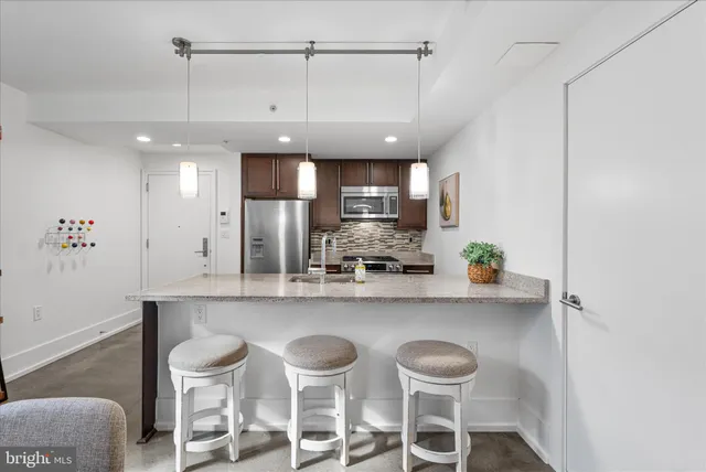 a kitchen with stainless steel appliances kitchen island granite countertop a refrigerator a stove a sink and a dining table with white cabinets