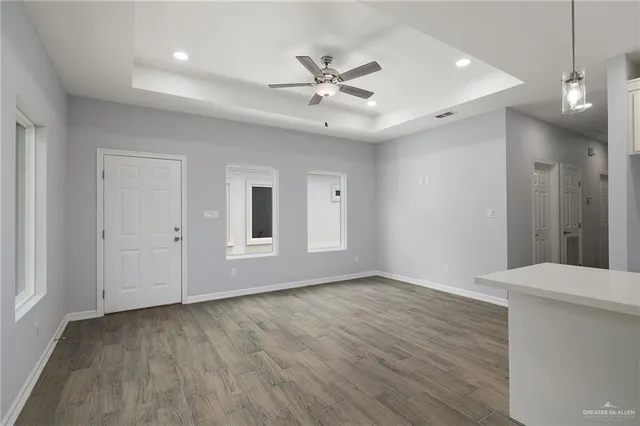 a view of an empty room with wooden floor and a ceiling fan