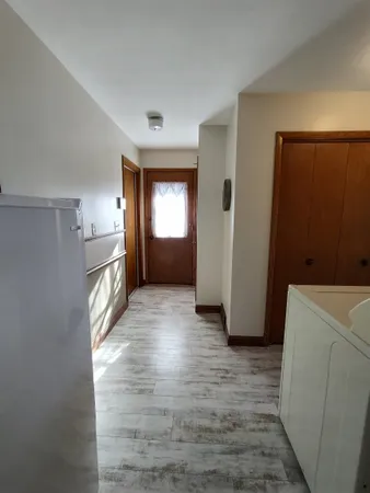 a view of a hallway to an empty room with wooden floor and a window