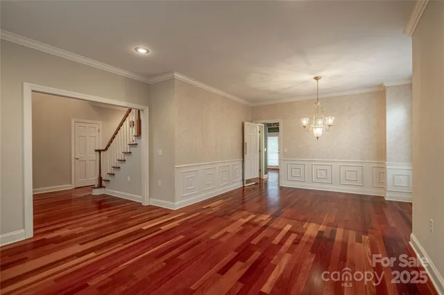 a view of an empty room with wooden floor stairs and a chandelier