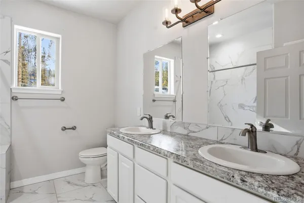 a bathroom with a granite countertop double vanity sink a mirror and a toilet